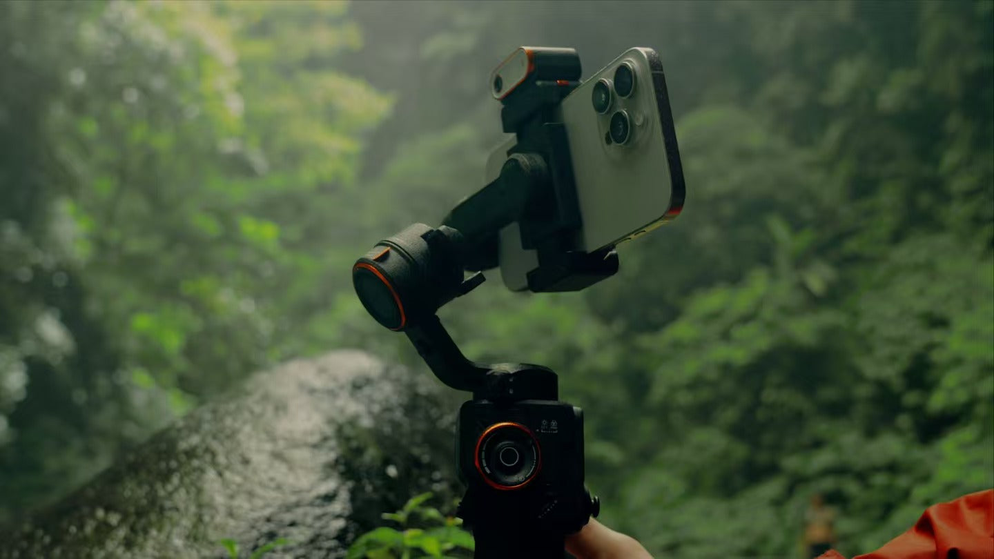 A smartphone mounted on a gimbal stabilizer in a lush, green outdoor setting, capturing steady footage in a natural environment.