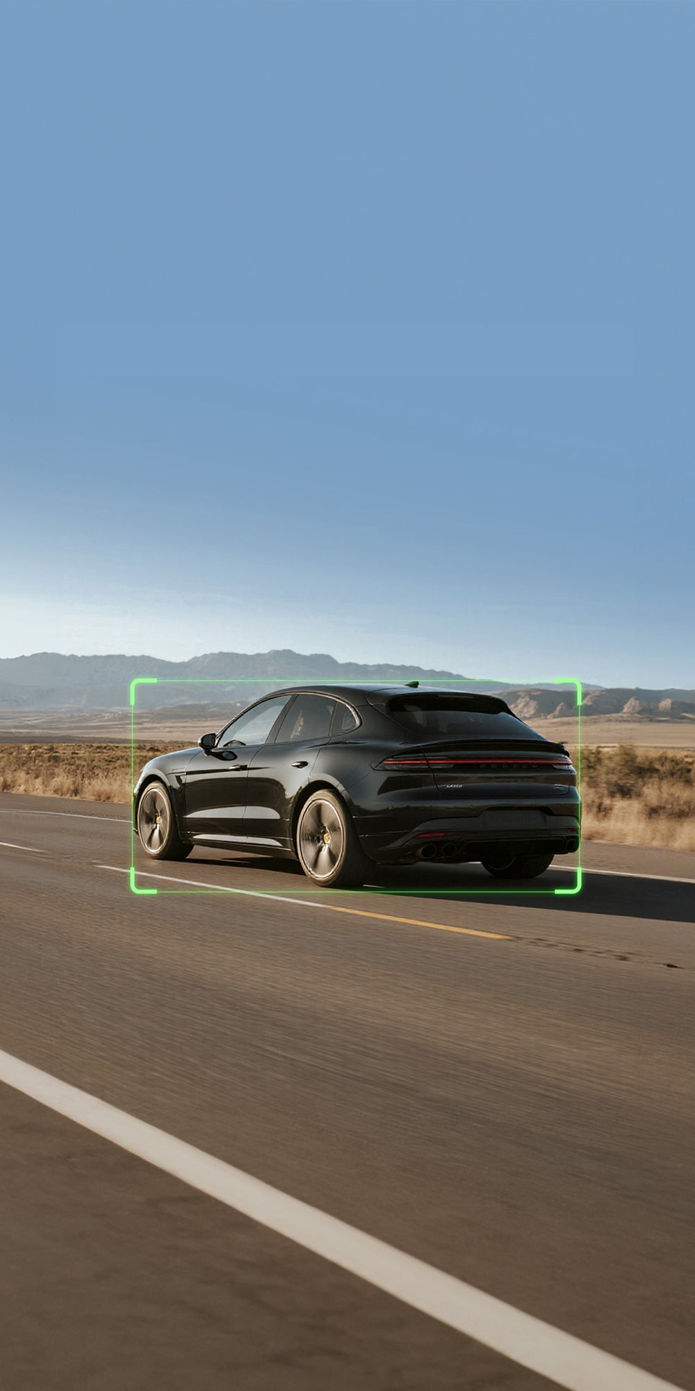 Black SUV driving on a road with a clear blue sky and mountains in the background.