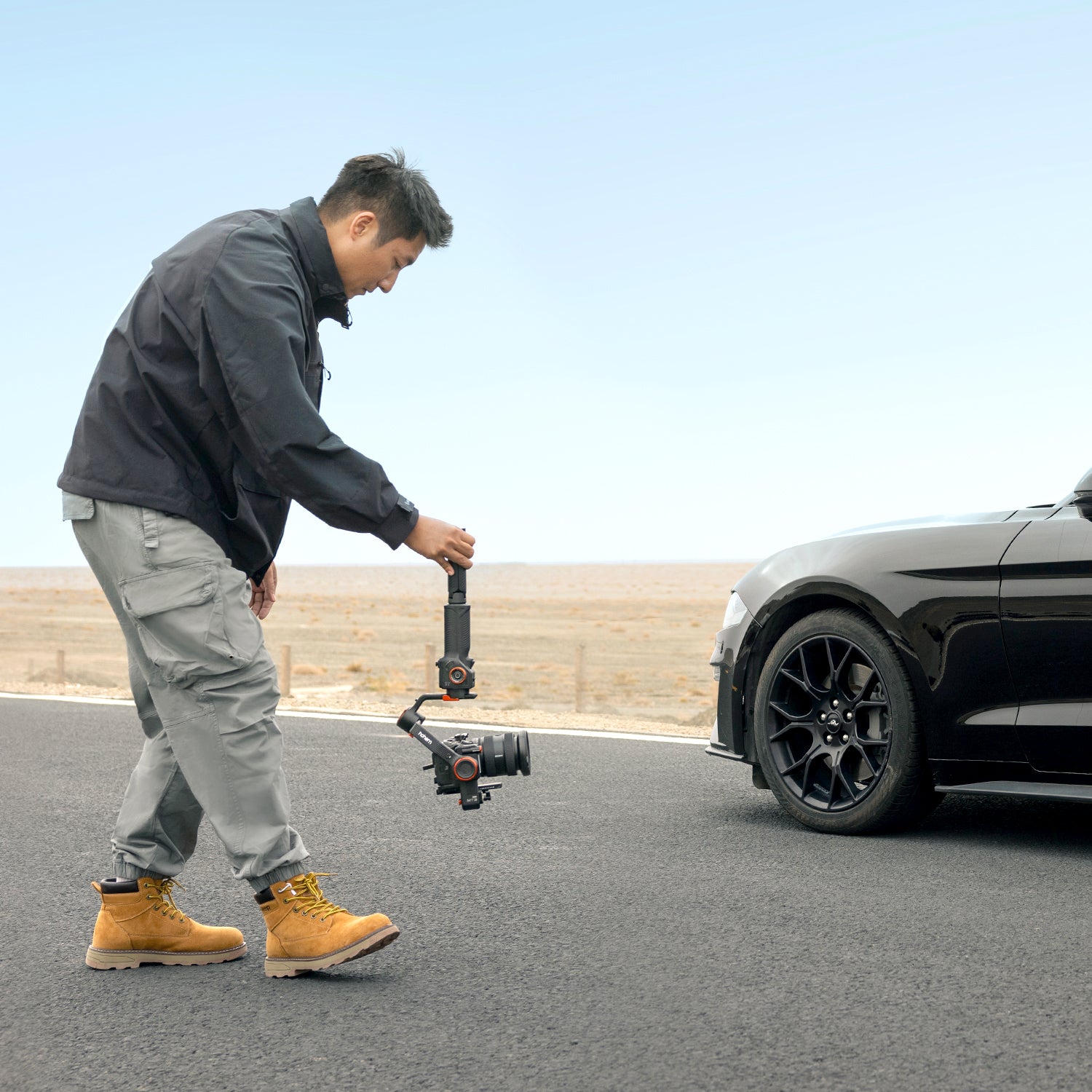 Person using a camera stabilizer on a road with a car in the background