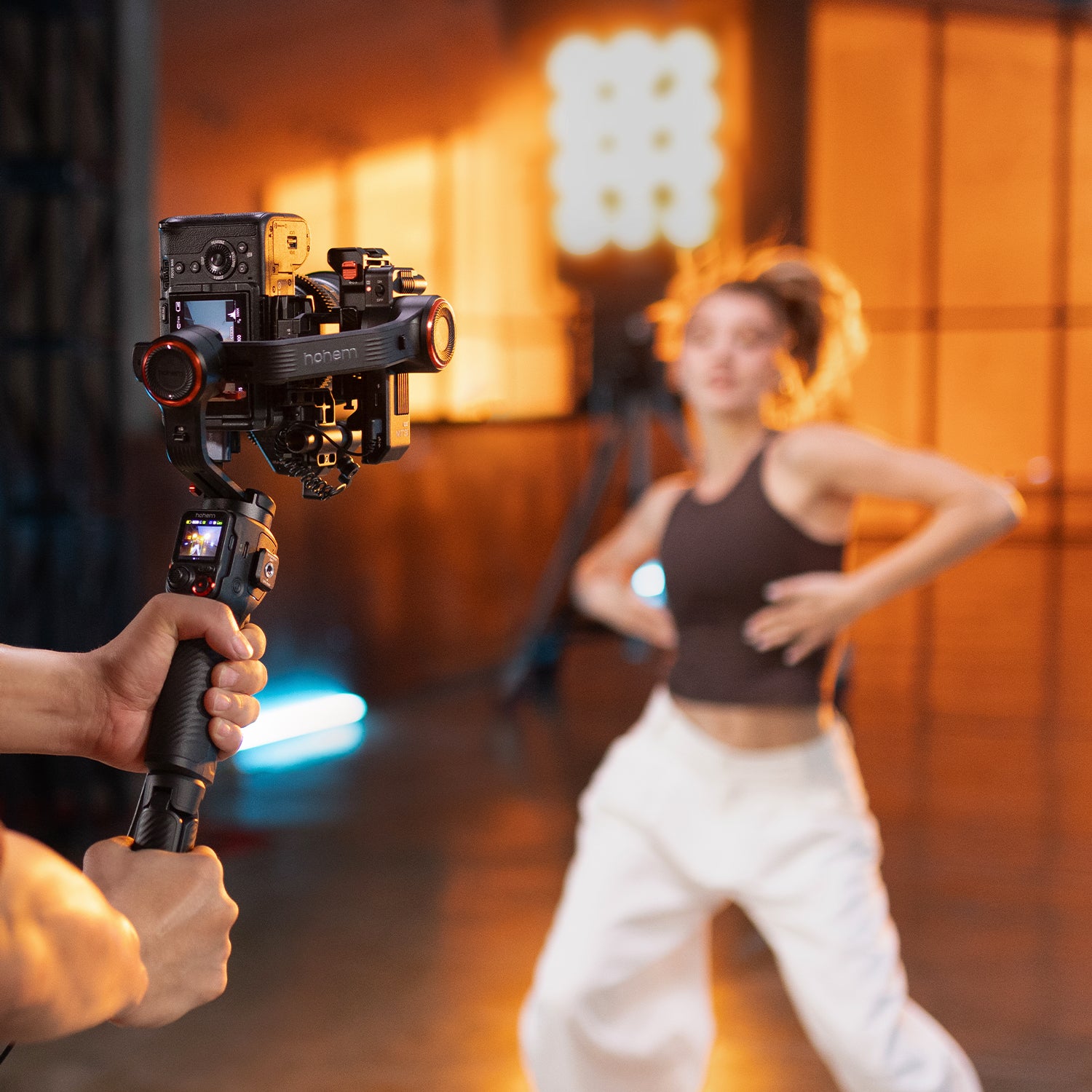 Person holding isteadymt3 pro camera stabilizer with a woman in the background in a studio setting