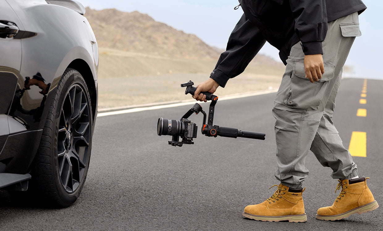 Person holding a camera stabilizer on a brief case mode while in the road with a car in the background